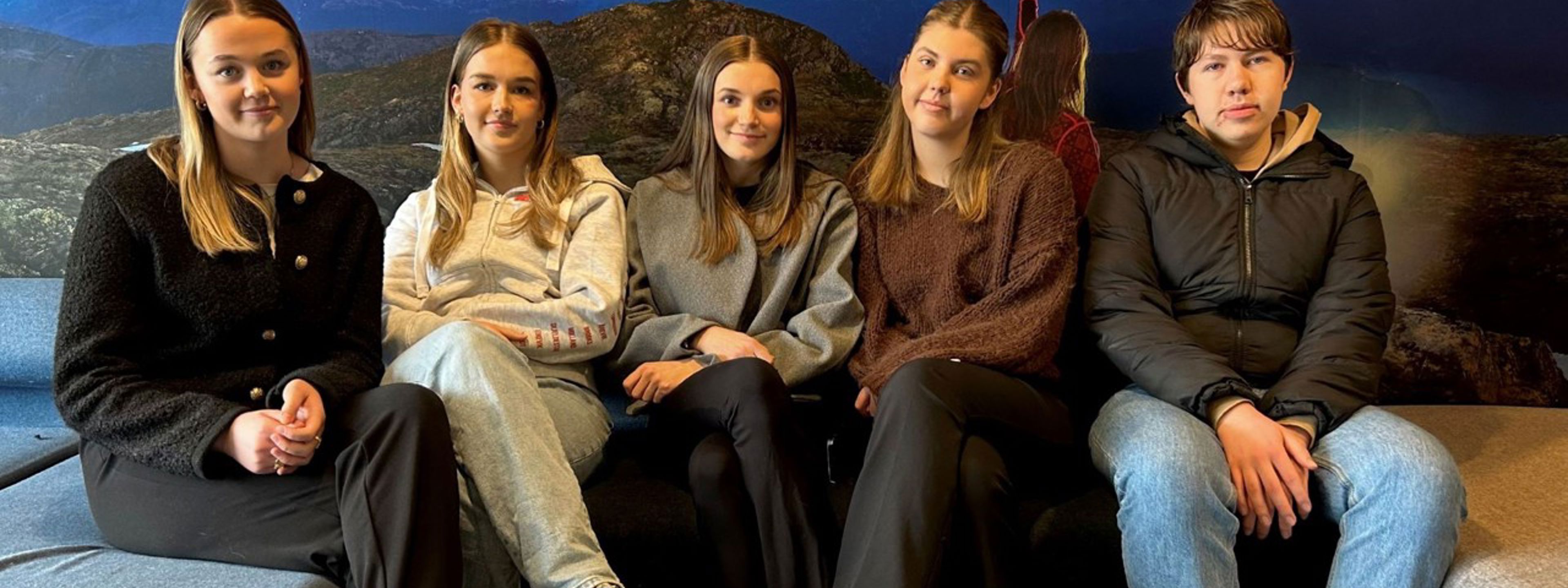 Fem smilande elevar sit tett i ein sofa. 